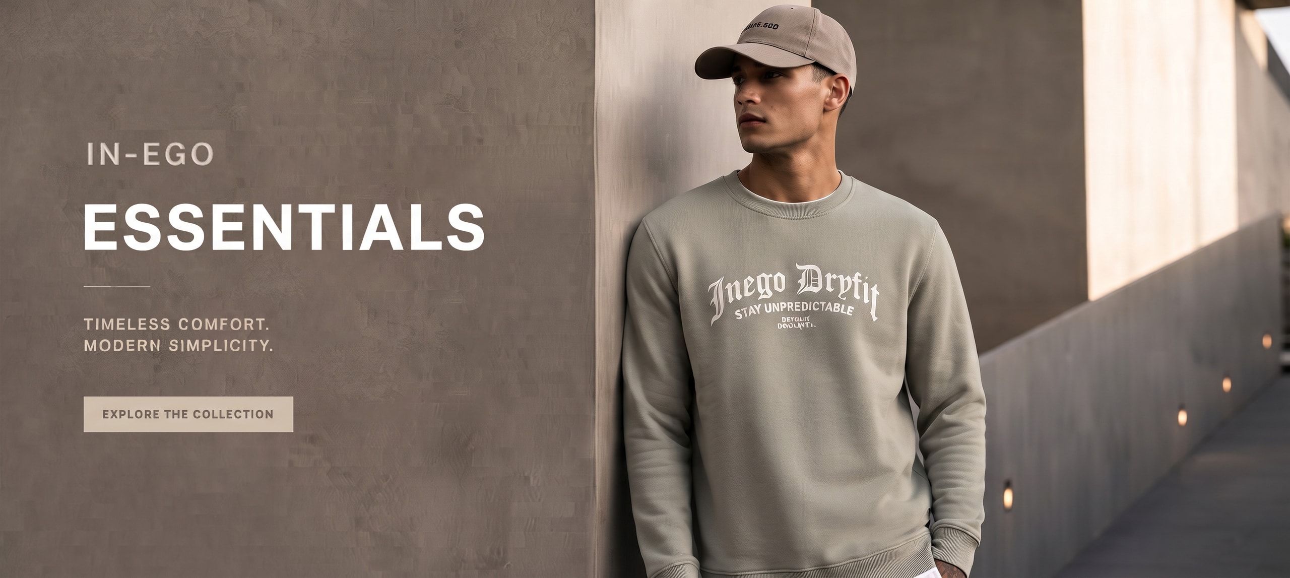 A man in a beige cap leaning against a concrete wall, wearing a sage-green “Inego Dryfit” crewneck sweatshirt printed “Stay Unpredictable”, beside the words “IN-EGO Essentials - Timeless comfort. Modern simplicity. - Explore the collection”.